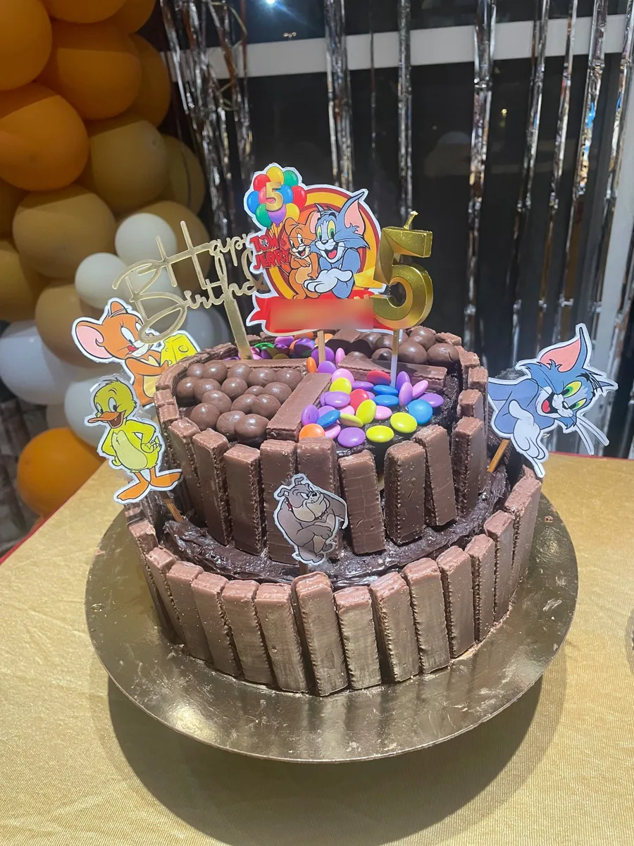 A two-tier chocolate birthday cake ringed with chocolate wafers, topped with chocolate balls and gems