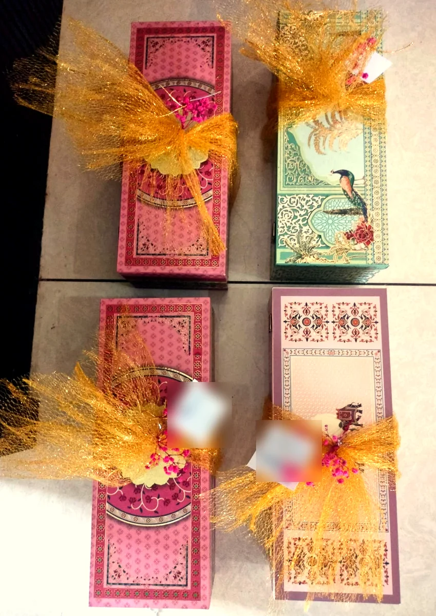 Four printed gift boxes wrapped in gold mesh with pink dried flowers and client greeting tags